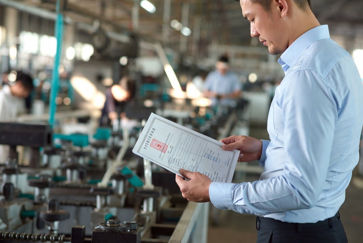 China sourcing agent in a factory with a paper clipping on his hand