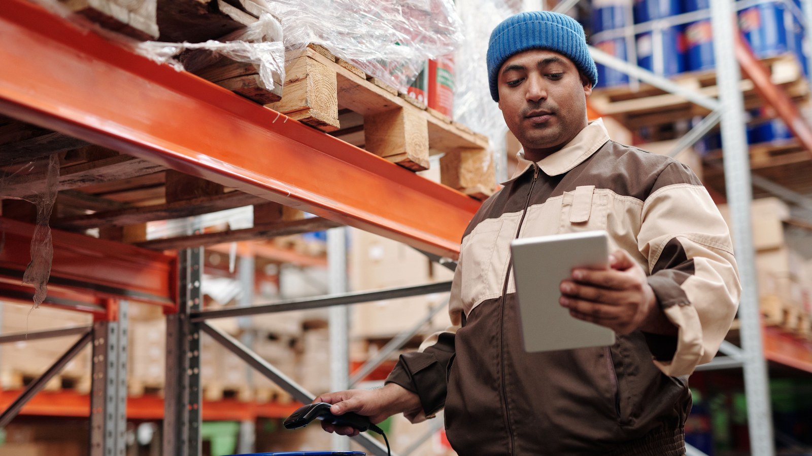 A worker scanning cartons with a handheld device in a warehouse aisle.