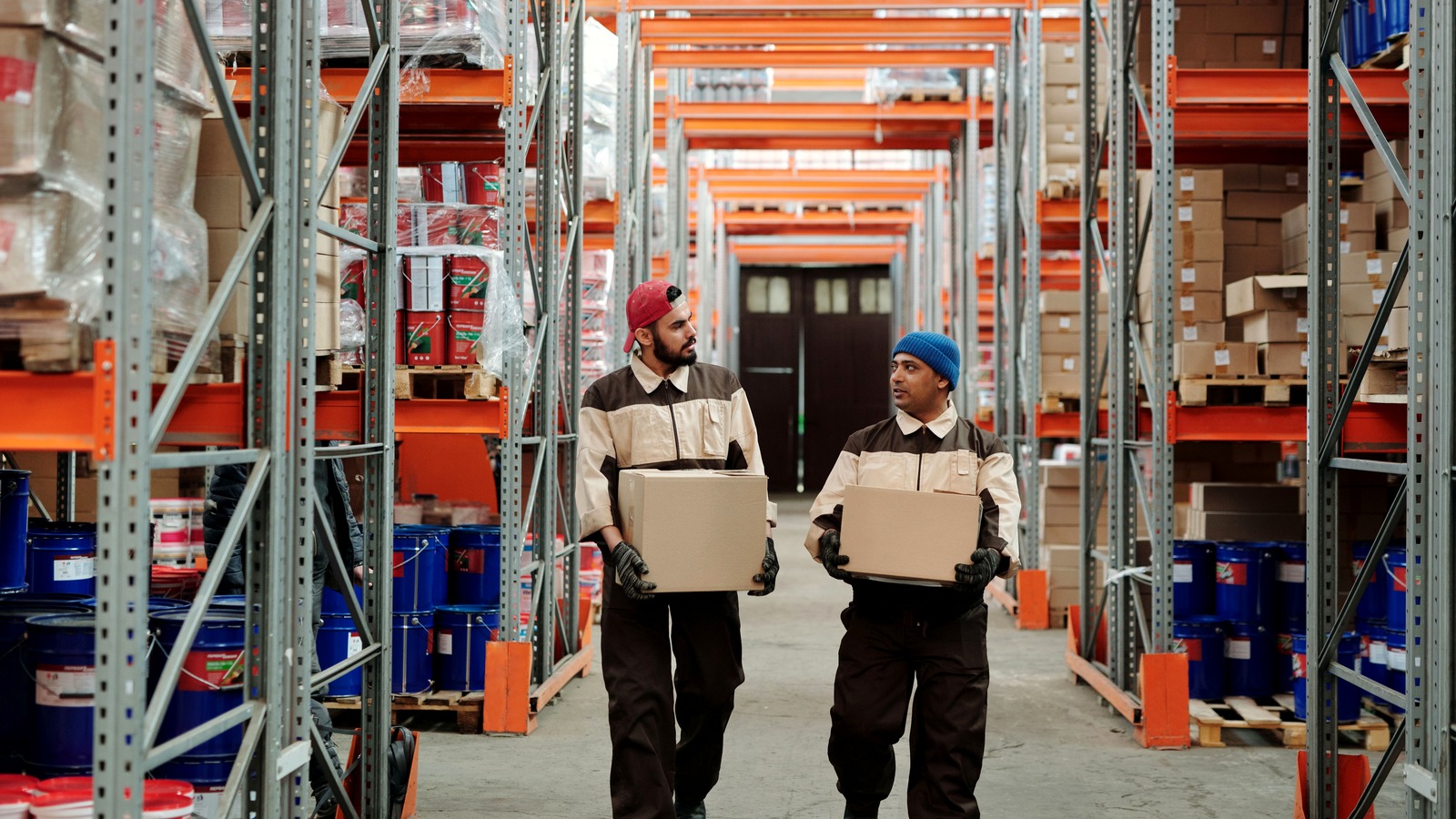 Two warehouse workers carrying cardboard cartons along a racked aisle in a China export fulfilment warehouse, illustrating low-value parcels prepared for export to the United States that must be declared to US Customs and Border Protection under the proposed Low-Value Shipments rule.
