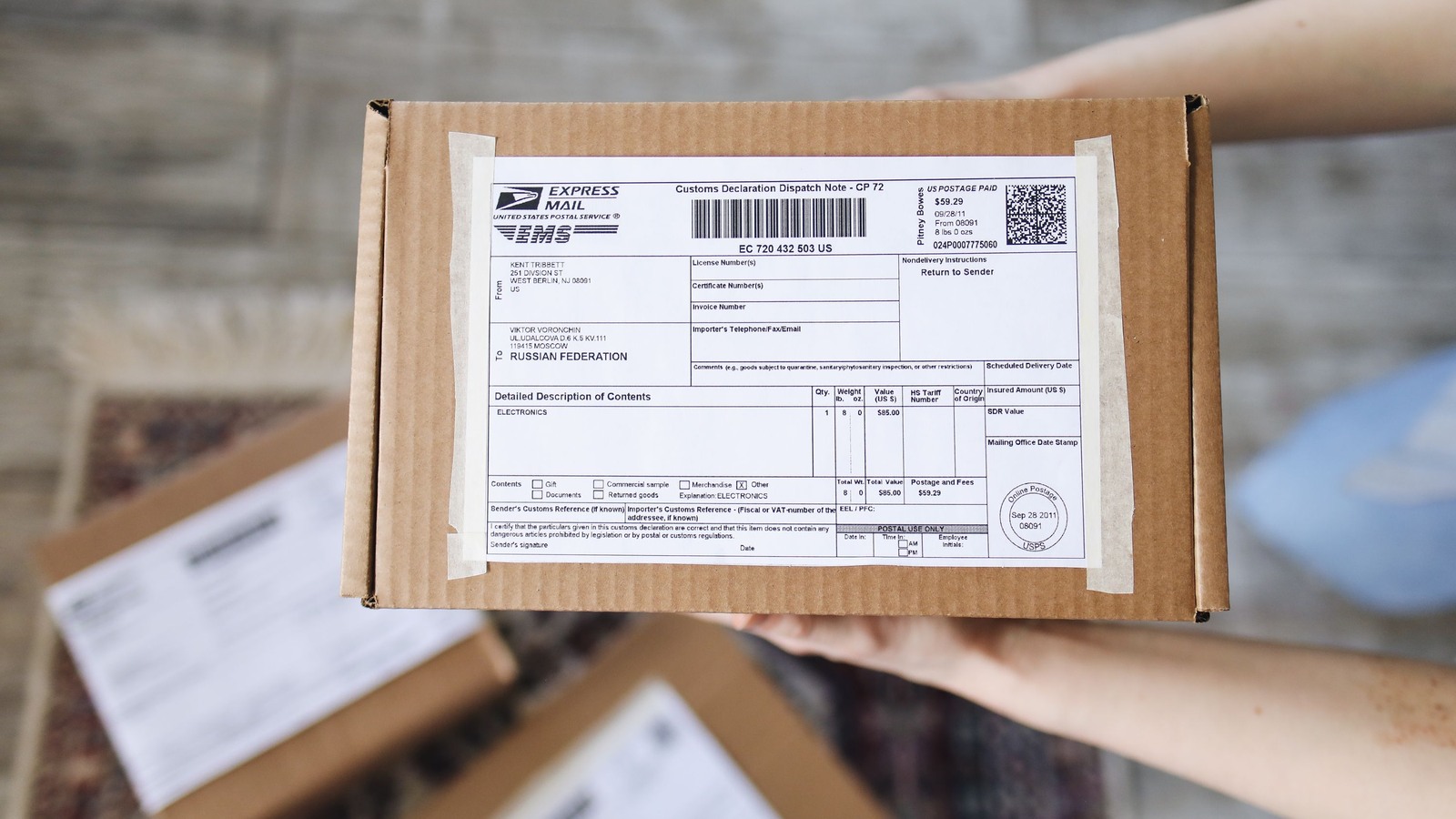 A hand holding a China export mail parcel with a Customs Declaration Dispatch Note attached, showing the country of export, description of contents, gross weight and postal tracking number that US Customs and Border Protection requires for entry type 13 informal mail entries.