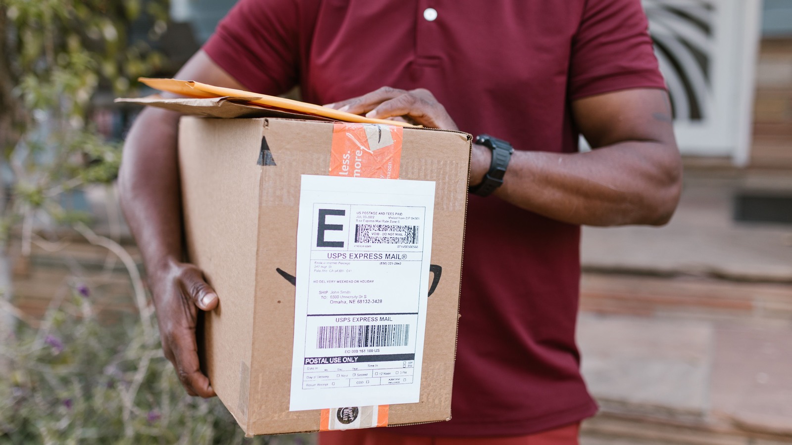 A courier holding a parcel bearing a USPS Express Mail tracking label and barcode, illustrating the US postal channel and the tracking number that must match across the declaration, the carrier manifest and the parcel under the proposed entry type 13 rules.